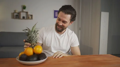 A young man sits at a table and talks about the usefulness of fruits, he picks Vídeo Stock 128006427