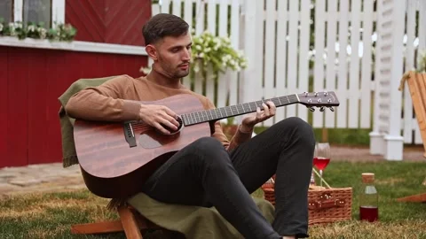 Young man sits at the table and plays the guitar Stock Footage 254122521
