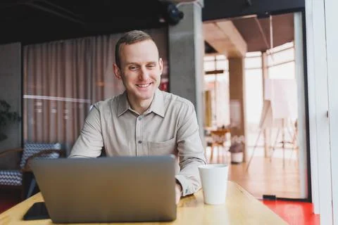 A young man sits at a table and opens a laptop computer while studying online Stock Photos