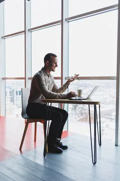 A young man sits at a table and opens a laptop computer while studying online Stock Photos