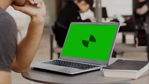 Young man sits at a table in a cafe at a laptop with a mockup green screen and Stock Footage 252896924