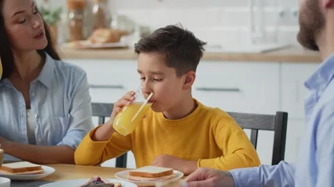 A young man sits at a table with his parents and drinks orange juice. A boy in Stock Footage 240318462