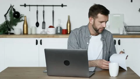 A Young Man Sits at a Table at Home and Working on a Laptop Writes down Notes Stock Footage 156962908