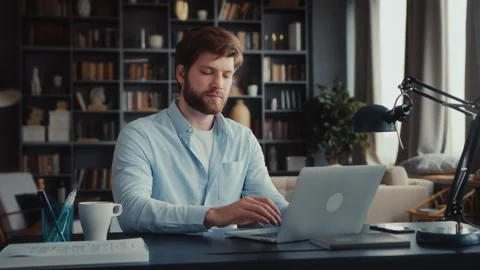 Young man sits at table with laptop in home office Stock Footage 260933476