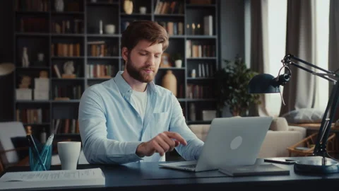 Young man sits at table with laptop in home office Stock Footage 260933729