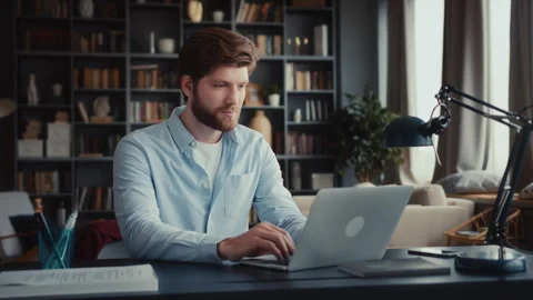 Young man sits at table with laptop in home office Stock Footage 260936524