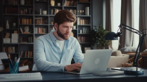 Young man sits at table with laptop in home office Stock Footage 260936564