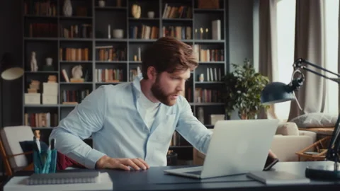 Young man sits at table with laptop in home office Video stock 261132847