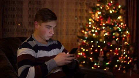 A young man sits with a tablet in him hands on the background of a Christmas Stock Footage 121232944