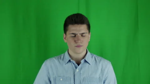 Young man sits thinking and scatches head in front of greenscreen Vidéo 59090934