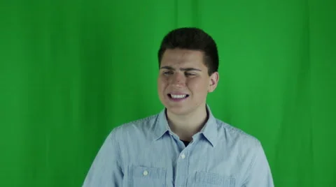 Young man sits thinking and shrugs in front of greenscreen Vidéo 59091878