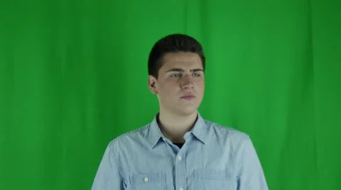 Young man sits uncomfortably in front of a greenscreen in a blue shirt Vidéo 59085431