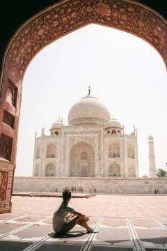 Young man sits under gate and looks at Taj Mahal in Agra Foto stock