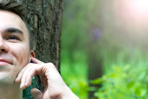 A young man sits under a tree and listens to music 스톡 사진