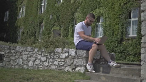 Young man sits on the wall and starts writing on laptop. 库存影片 65524676