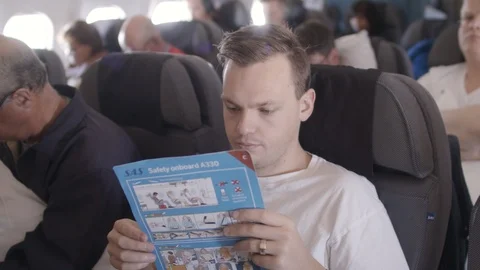 Young man sitting on an airplane, reading the safety manual Stock Footage 116023736