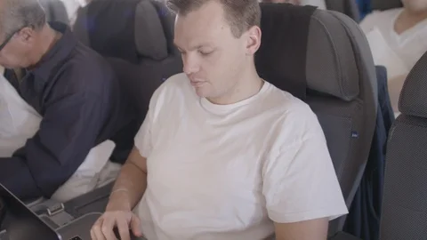 Young man sitting on an airplane, working on his computer Stock Footage 116023477
