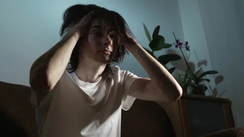 Young man sitting alone in dim room lost in heavy thoughts yet finding strength Stock Footage 331206379