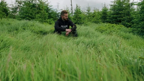 Young man sitting alone on the ground in the forest, nature in the mountains 4K. Video stock 234564736