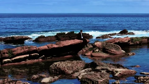 Young man sitting alone on large rock near ocean waves. Teenager resting quietly Stock Footage 313266857