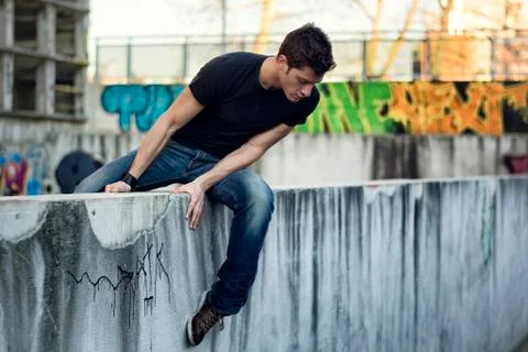 Young man sitting and balancing on wall, looking down Stock Photos