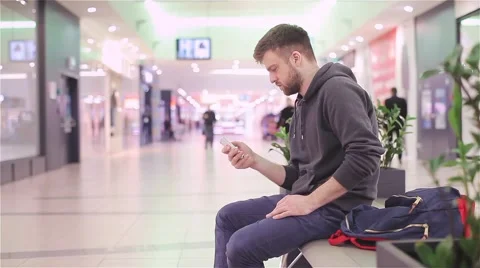 Young Man Sitting and Looking at the Phone in a Mall. Stock Footage 47977340