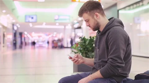 Young Man Sitting and Looking at the Phone in a Mall. Stock Footage 47977353