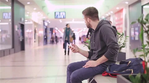Young Man Sitting and Looking at the Phone in a Mall. Stock Footage 47977357