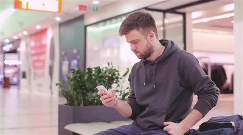 Young Man Sitting and Looking at the Phone in a Mall. Stock Footage 47977363