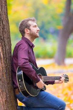 Young man sitting and playing acoustic guitar Фото