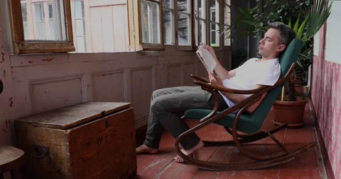 Young man sitting and reading in rocking chair Stock Footage 130646695