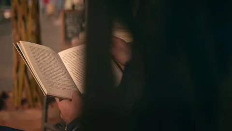 A young man is sitting and reading a book in a cafe on the street Stock Footage 139783987