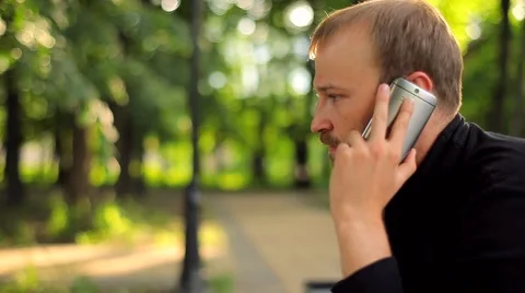 The Young Man Sitting and Talking on the Phone in the Park Video stock 50994834