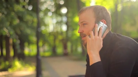 The Young Man Sitting and Talking on the Phone in the Park Stock Footage 50994842