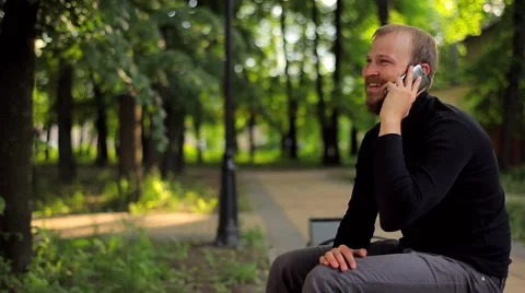 The Young Man Sitting and Talking on the Phone in the Park Stock Footage 50994851