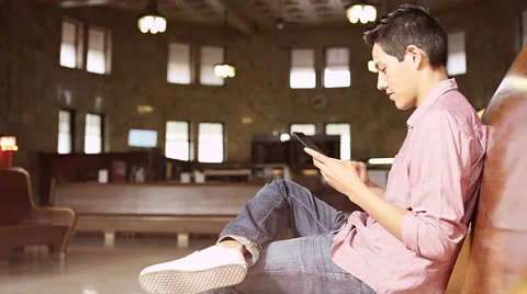 A young man sitting and using a tablet at a railroad terminal 库存影片 57509780