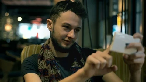 Young man sitting in the armchair and doing selfies on smartphone Stock Footage