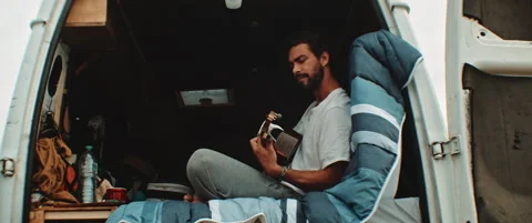 Young man sitting in the back of a van playing the guitar and singing Stock Footage 203584202
