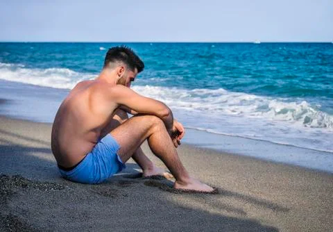Young man sitting on a beach alone and lonely Stock Photos