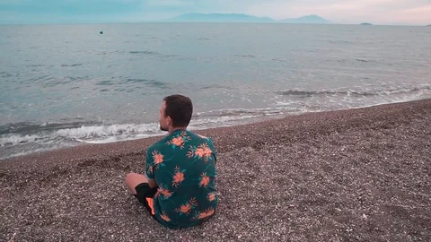 Young man sitting on the beach and  throwing pebbles into the sea.  Stock-Footage 109292322