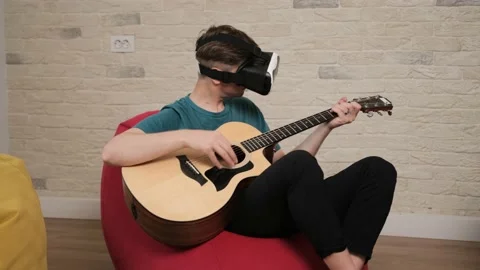 Young man sitting on bean bag with the vr glasses is playing at the guitar. Stock Footage 141448051
