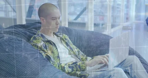 A young man is sitting in a beanbag and using a laptop computer in a modern open Stock Footage 328311441