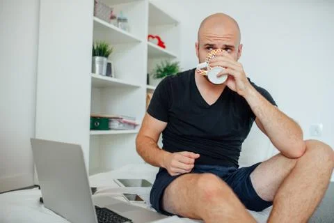 Young man is sitting on the bed and drinking something from a mug. Stock Photos