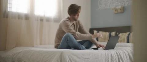 A young man sitting in bed with laptop, working from home, medium shot Stock Footage 135095219