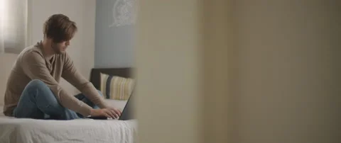 A young man sitting in bed with laptop, working from home Stock Footage 135095230
