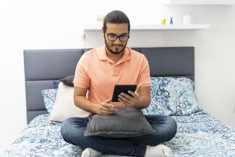 Young man sitting on bed reading on a e reader Stock Photos