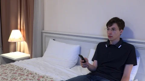 Young man sitting on bed with remote watching TV Stock Footage 120308681