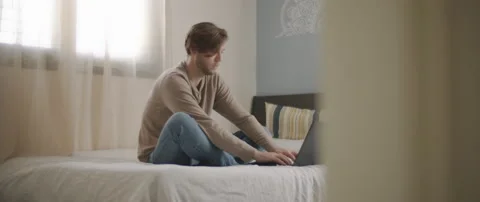 A young man sitting in bed, typing on laptop, working from home Stock Footage 135095220