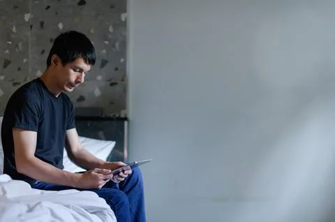 Young man sitting on bed using tablet in modern room Фото