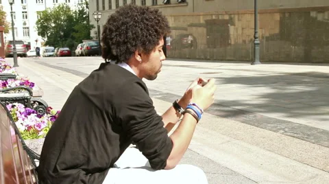 Young man sitting on the bench and texting  smartphone device. Stock Footage 54176464